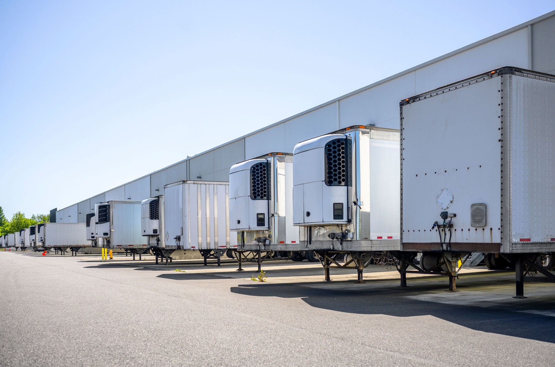 Different semi trailers without semi trucks standing at long warehouse dock gates for loading cargo for the next delivery